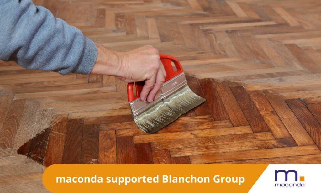 Hand applying finish to a parquet floor with a wide brush orange maconda banner at the bottom