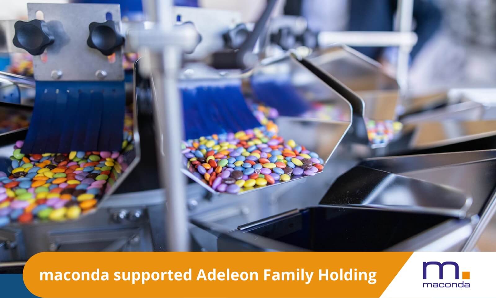 Industrial coating machine pouring colorful chocolate lentils onto a conveyor belt orange banner maconda supported Adeleon Family Holding