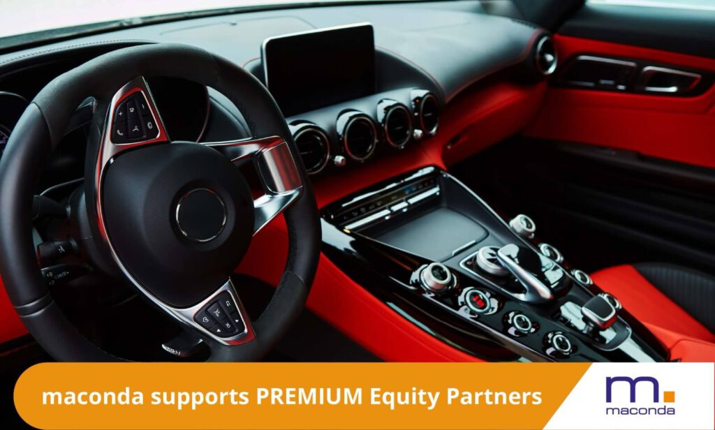 Interior of a luxury car with glossy center console and steering wheel orange banner maconda supports PREMIUM Equity Partners