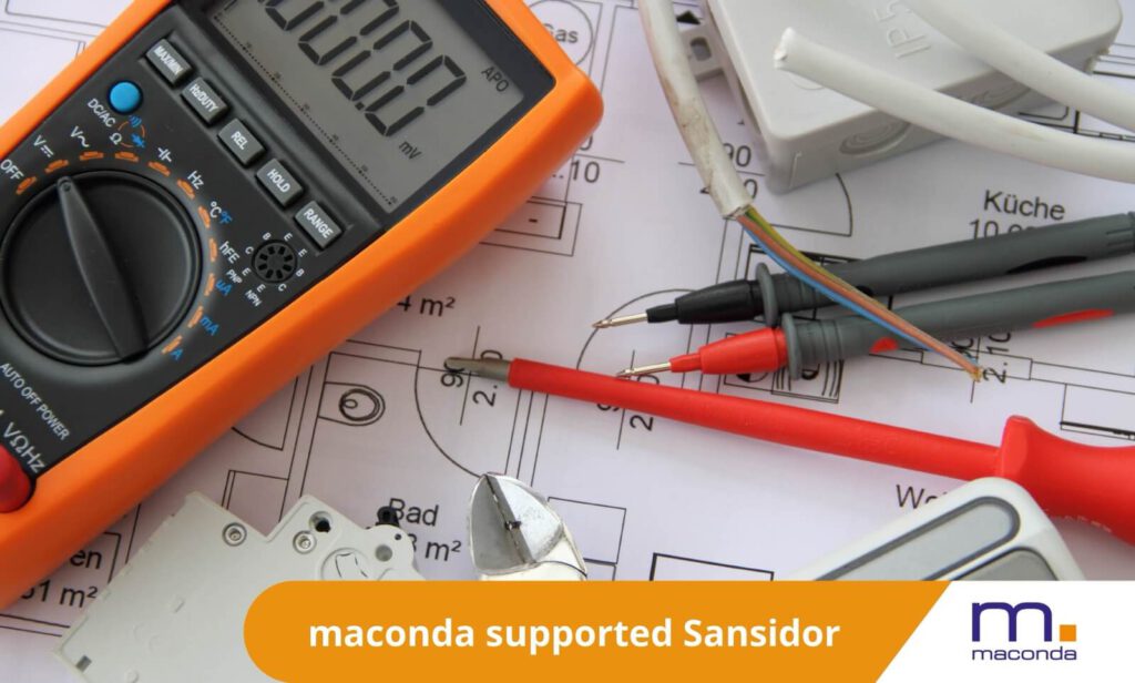 maconda News Dealbanner - Sansidor x flex_sec and GBS 250413 - maconda Orange digital multimeter with red and black test leads on a blueprint surrounded by electrical components and cables
