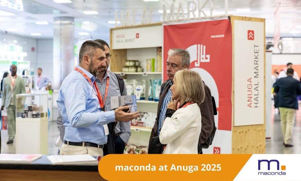 maconda News trade fair banner Anuga 251001 - maconda Four experts in conversation at a food industry trade fair stand in the foreground an orange banner reading maconda at Anuga 2025