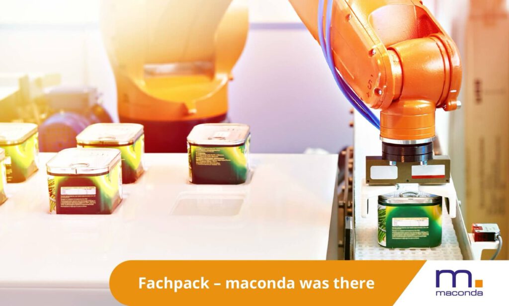 maconda News Trade Fair Banner Fachpack 250901 - maconda Orange industrial robot packaging green cans on a white conveyor belt FACHPACK branding in the foreground