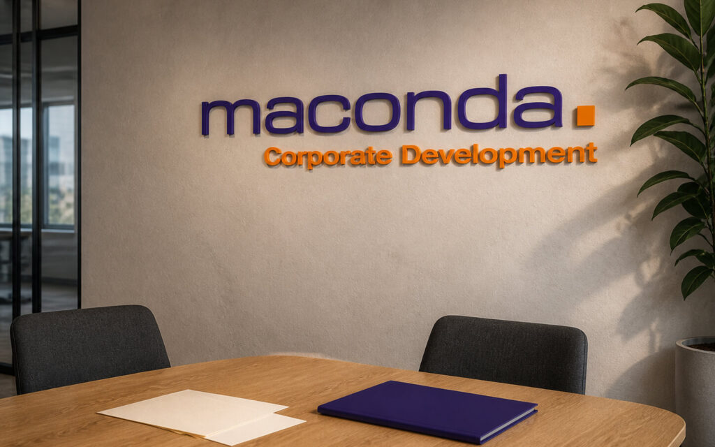 Meeting room with a beige wall purple maconda lettering and orange Corporate Development text a plant in the corner and a round wooden table with documents