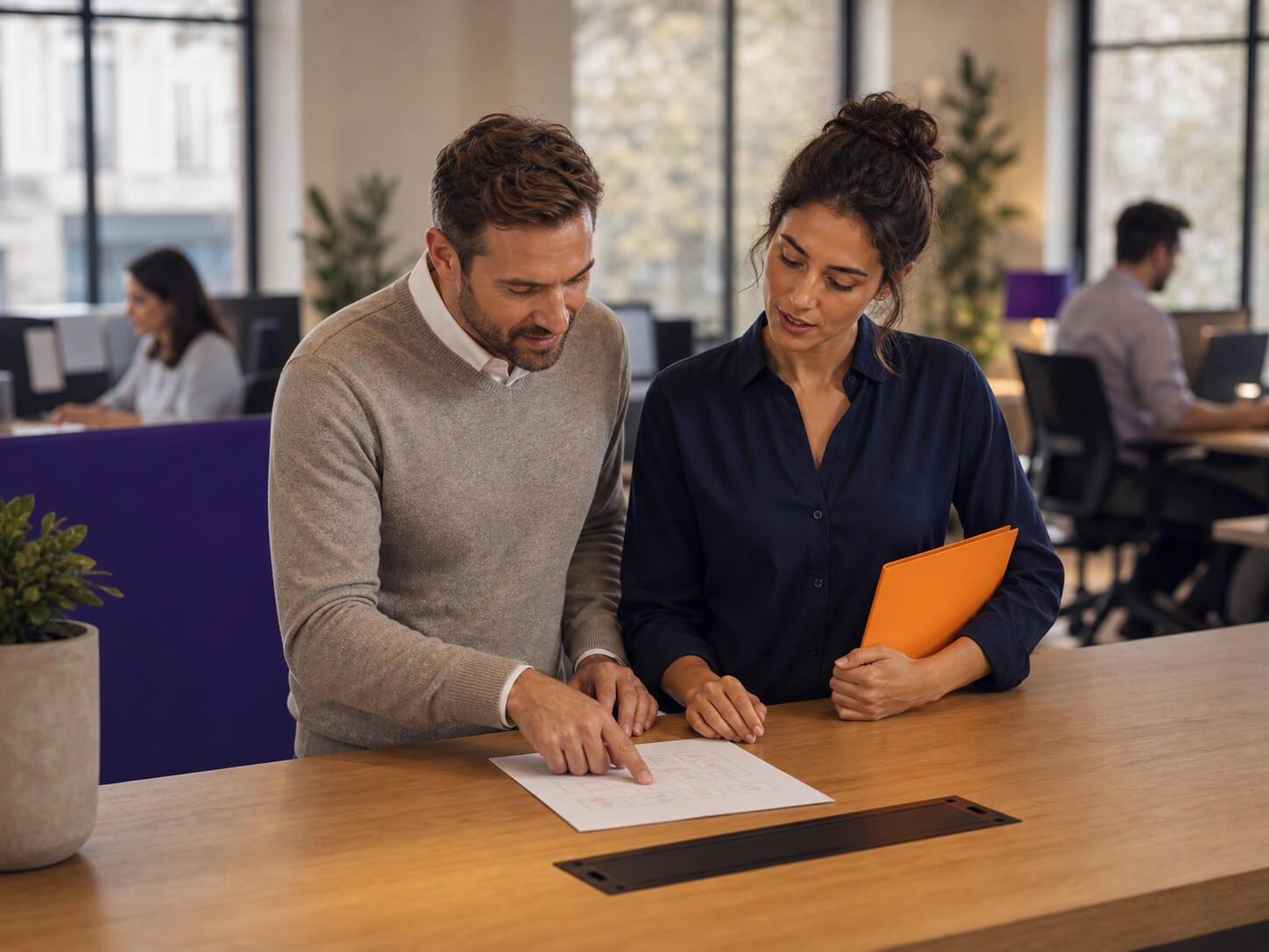 maconda-b2b-services-bpo - maconda Two colleagues review a plan together at a wooden desk in a modern open plan office