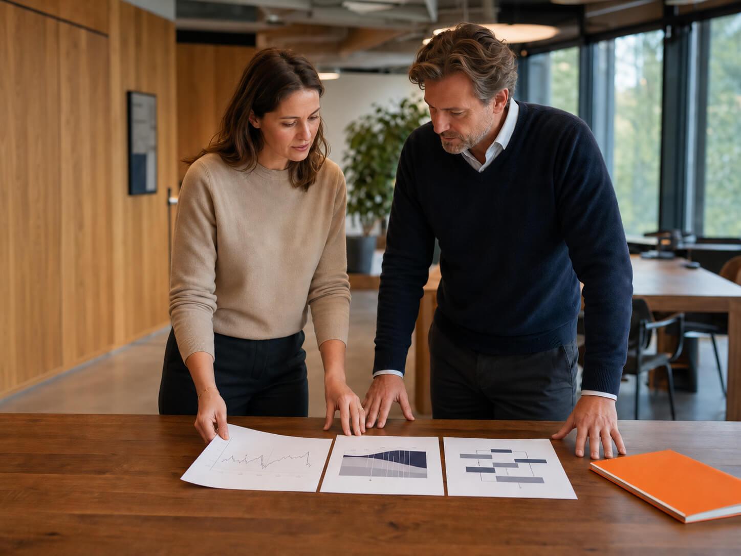 maconda-performance-management - maconda Zwei Kollegen besprechen Diagramme an einem Holztisch in einem hellen Büro