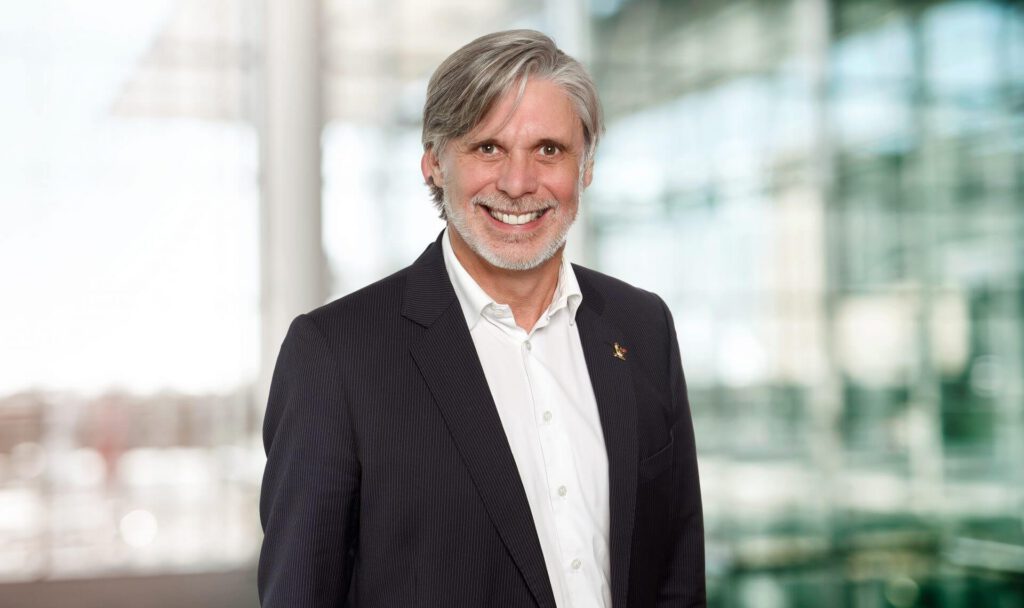 Portrait of Dr Rainer Mayer maconda in a dark pinstripe suit and white shirt smiling in a bright modern office