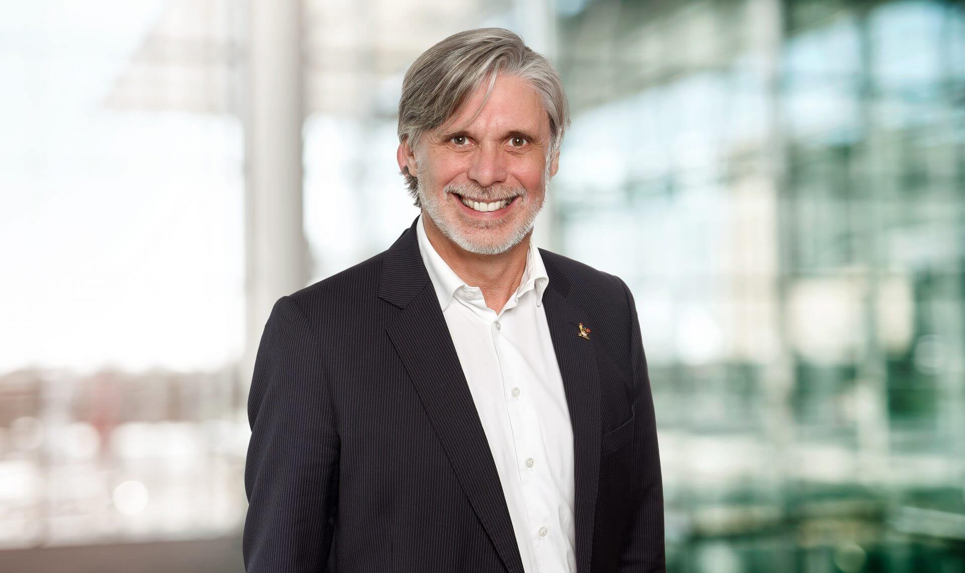 Portrait of Dr Rainer Mayer maconda in a dark pinstripe suit and white shirt smiling in a bright modern office