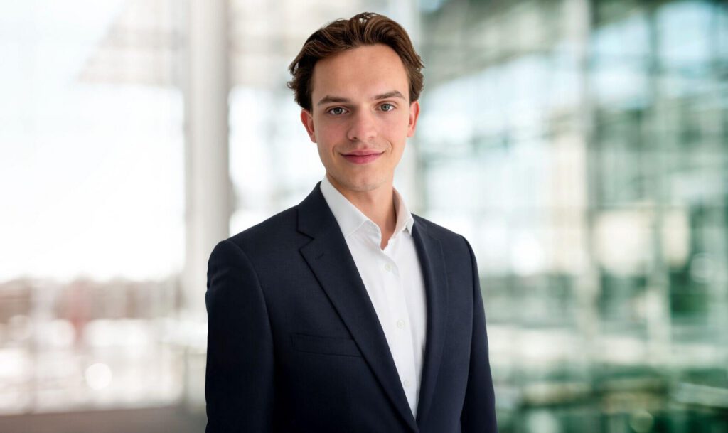 Porträt von Franz Kushnarev maconda in dunklem Anzug und weißem Hemd lächelnd in einem modernen Büro mit Glaswänden