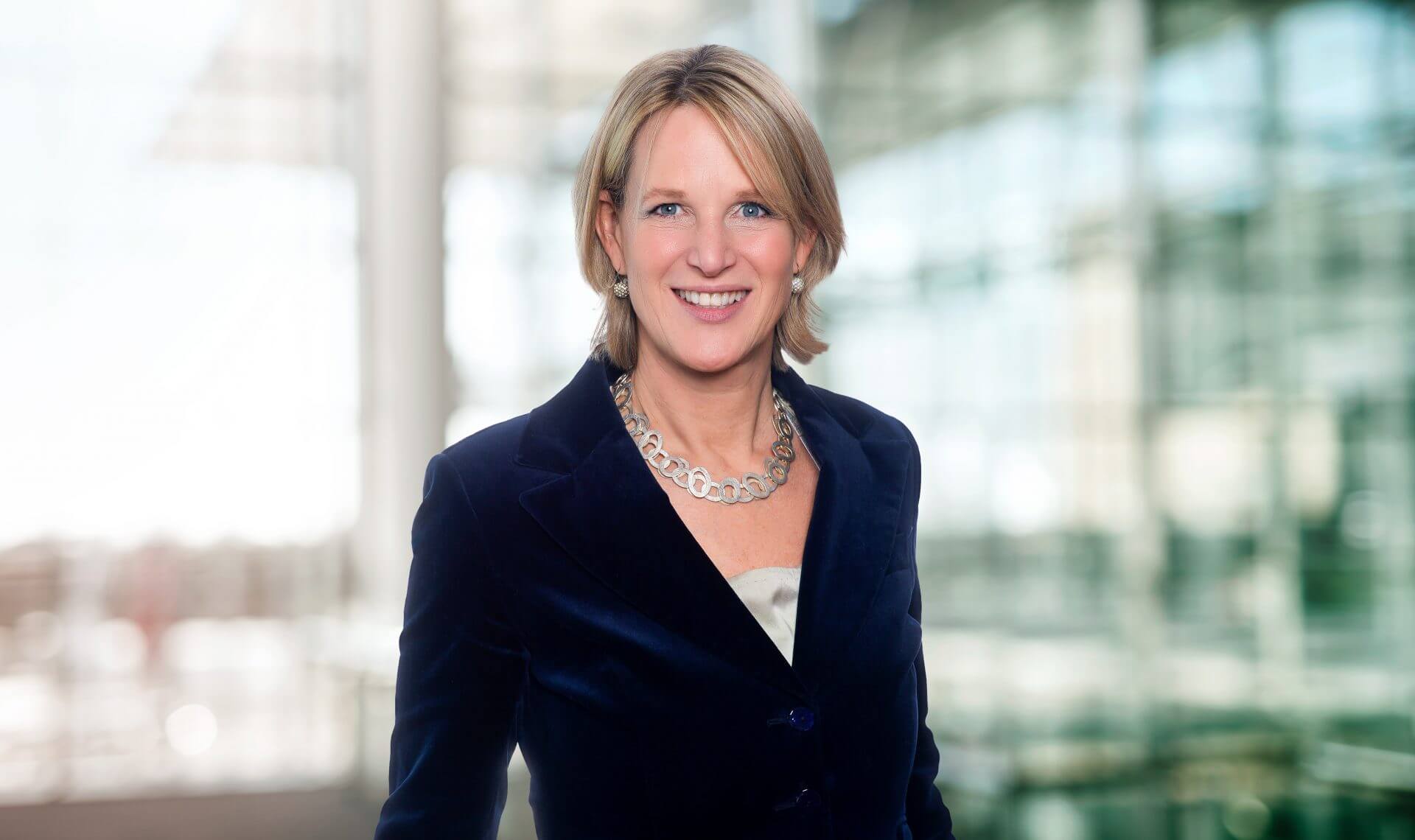Porträt von Isabelle Mayer Holtmann maconda in dunkelblauem Blazer mit silberner Halskette lächelnd in einem hellen Büro