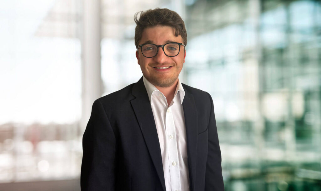 Porträt von Jonathan Stölting maconda mit dunklem Haar und Brille in schwarzem Blazer und weißem Hemd lächelnd in einem modernen Büro