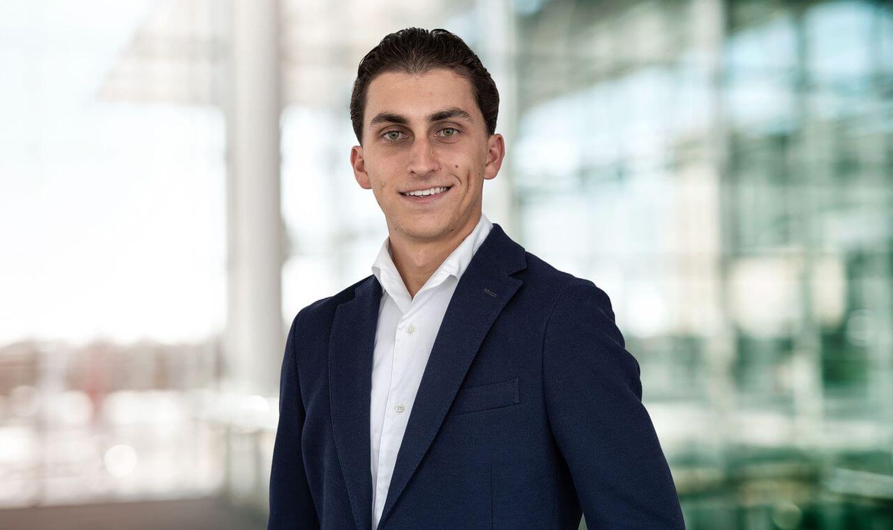 Porträt von Noah Bayazit maconda in dunkelblauem Blazer und weißem Hemd lächelnd in einer modernen Lobby mit Glaswänden