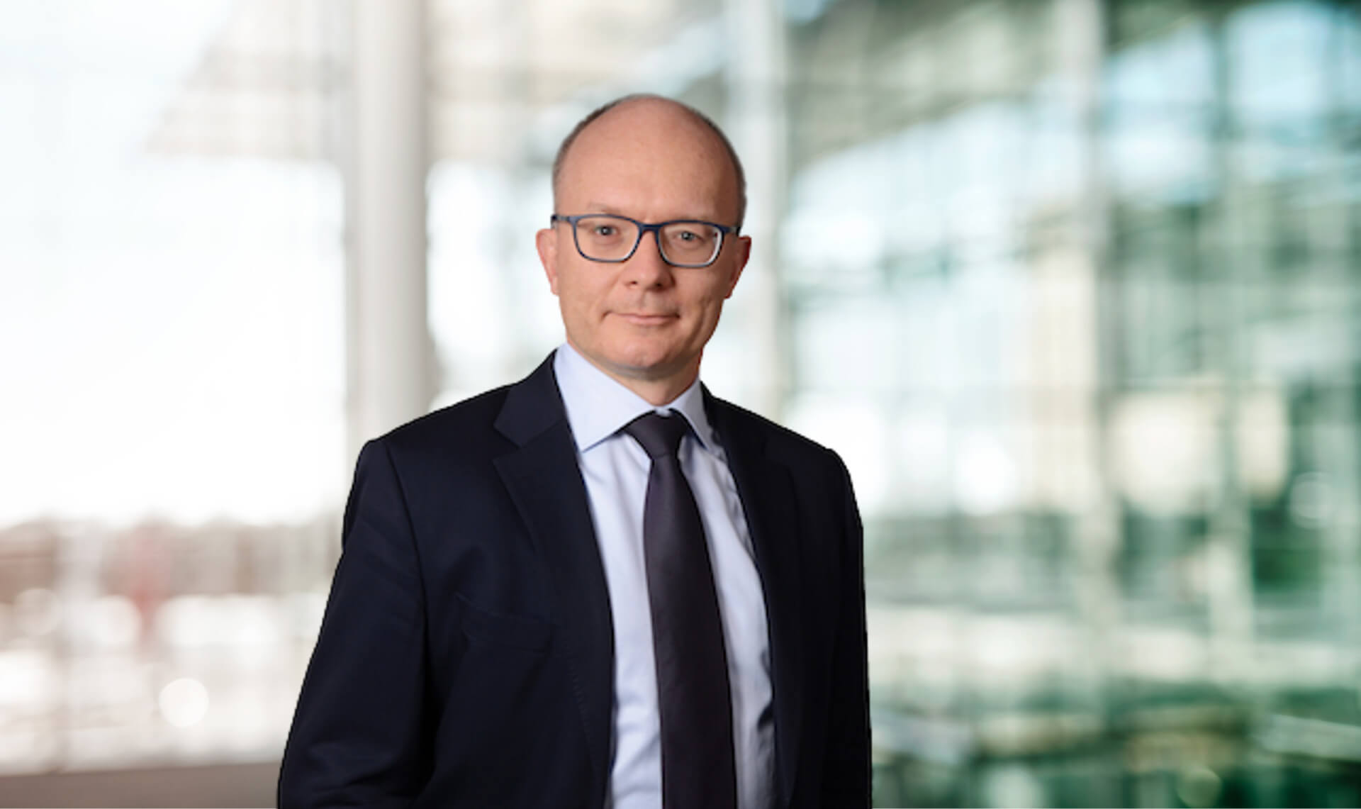 Porträt von Piotr Krzeszowiak maconda mit Brille in dunklem Anzug mit Krawatte in einer hellen modernen Lobby